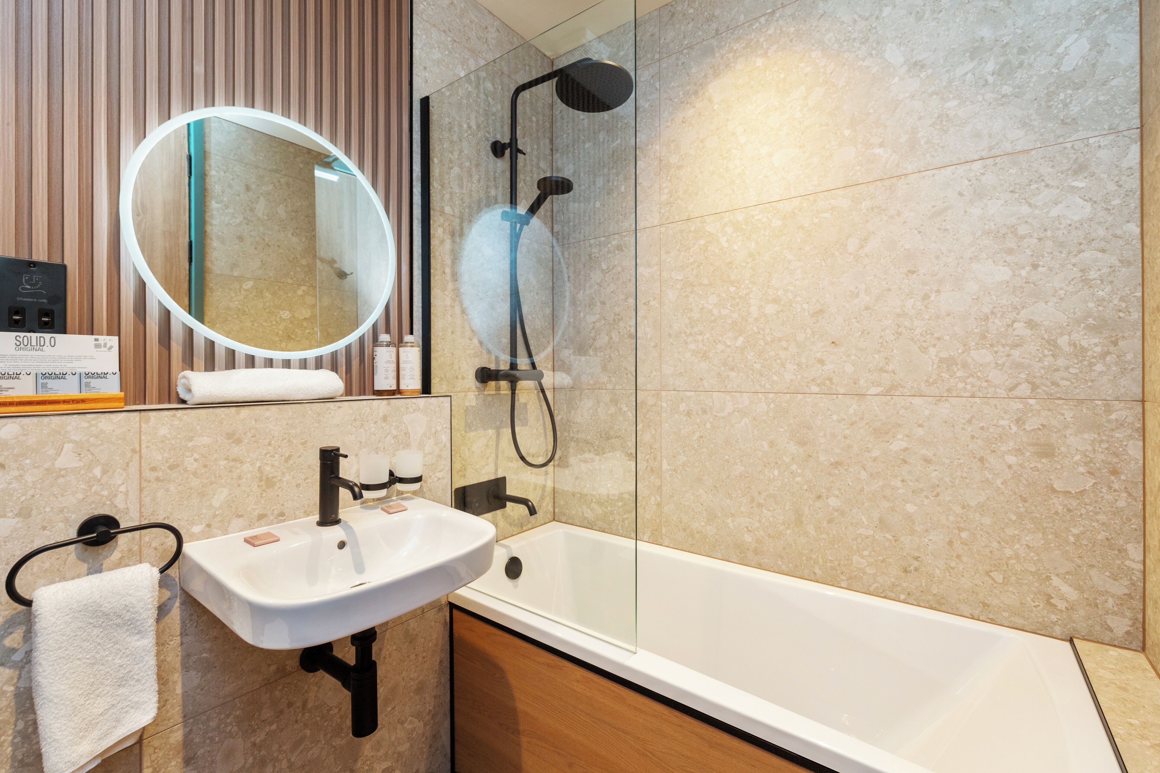 A modern bathroom with a white sink, a glass-enclosed shower, and a large mirror.