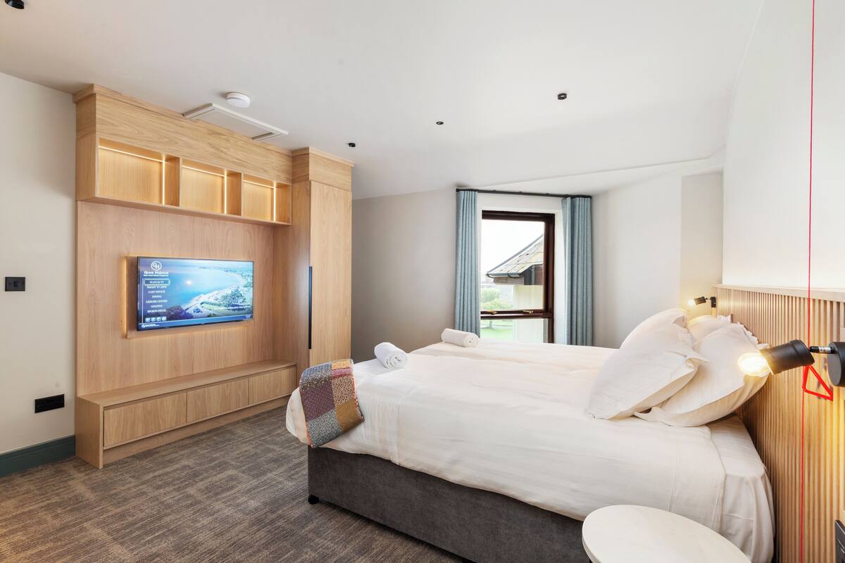 Une chambre d’hôtel moderne avec un grand lit, un téléviseur fixé au mur et une fenêtre avec des rideaux.