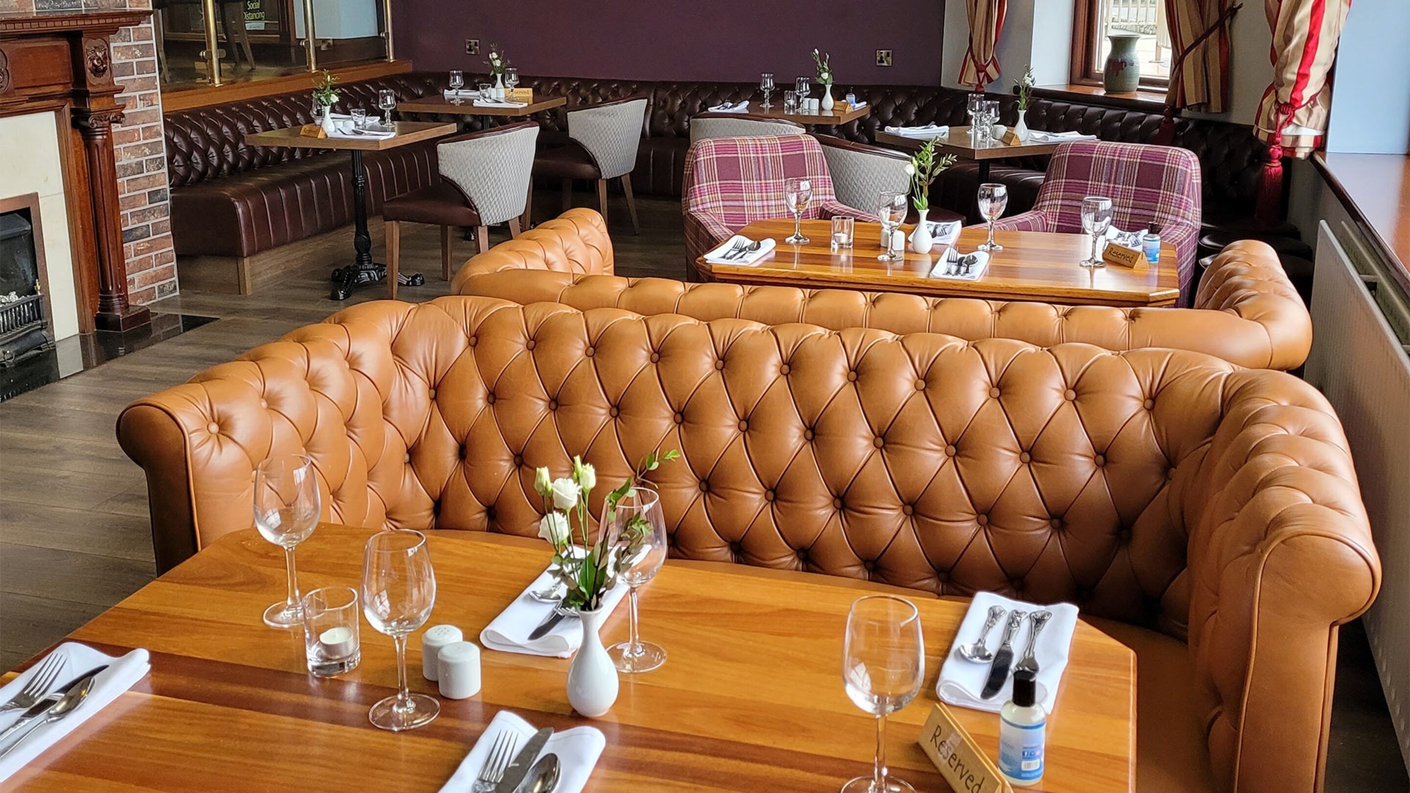 Een restaurant met lederen zitbanken, houten tafels en een bakstenen muur.