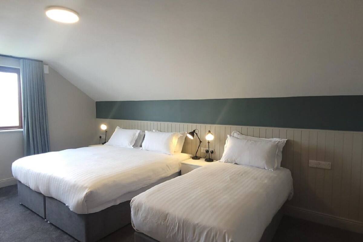 Une chambre d’hôtel avec deux lits, une fenêtre avec des rideaux et une tête de lit blanche.