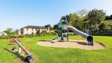 A playground with a slide, a climbing structure, and a seesaw.