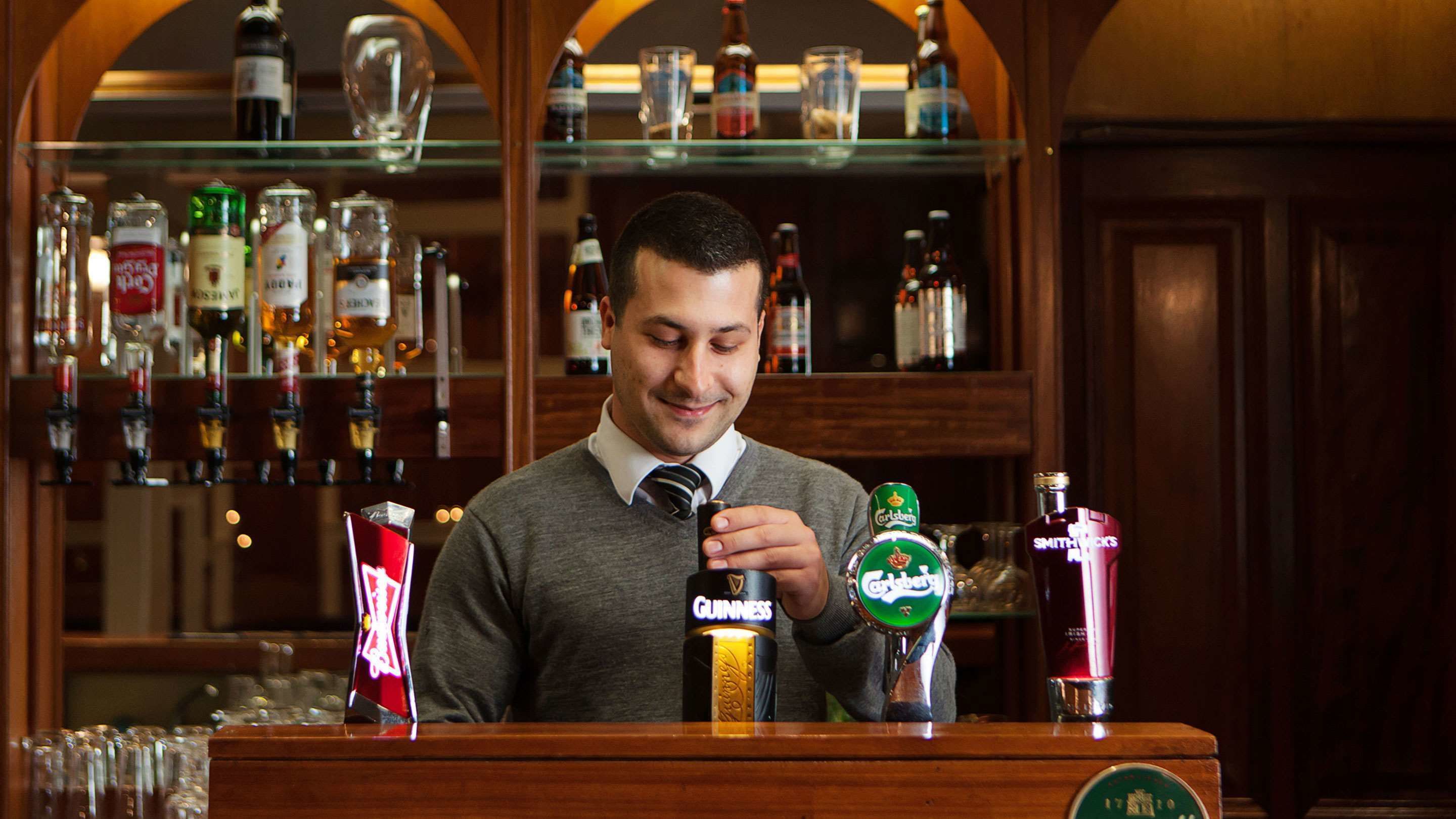A bartender pouring a drink from a Guinness bottle.
