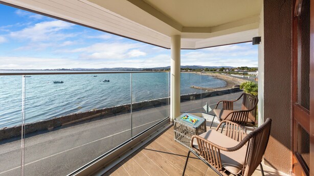 Un balcón con vista al mar, una mesa con sillas y una pequeña mesa con objetos encima.