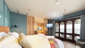 Habitación de hotel con una cama grande, televisión, escritorio con silla y vista al mar a través de un ventanal.