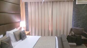 Une chambre d’hôtel avec un lit, une table de chevet, une lampe, une chaise et une vue sur l’extérieur à travers des rideaux.