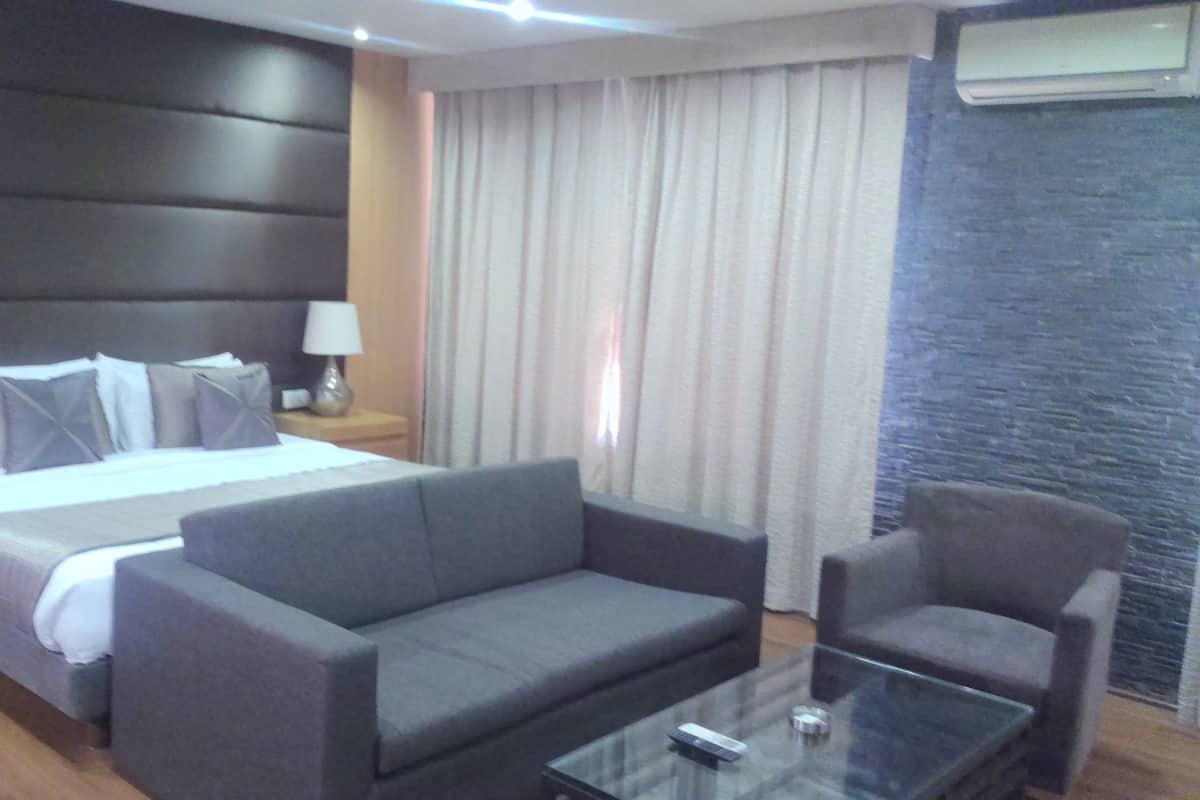 A hotel room with a bed, a sofa, a chair, a glass coffee table, and a lamp.