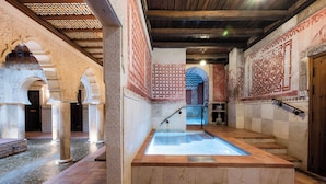 Un interior espacioso con una piscina central, arcos ornamentales y paredes de azulejos.