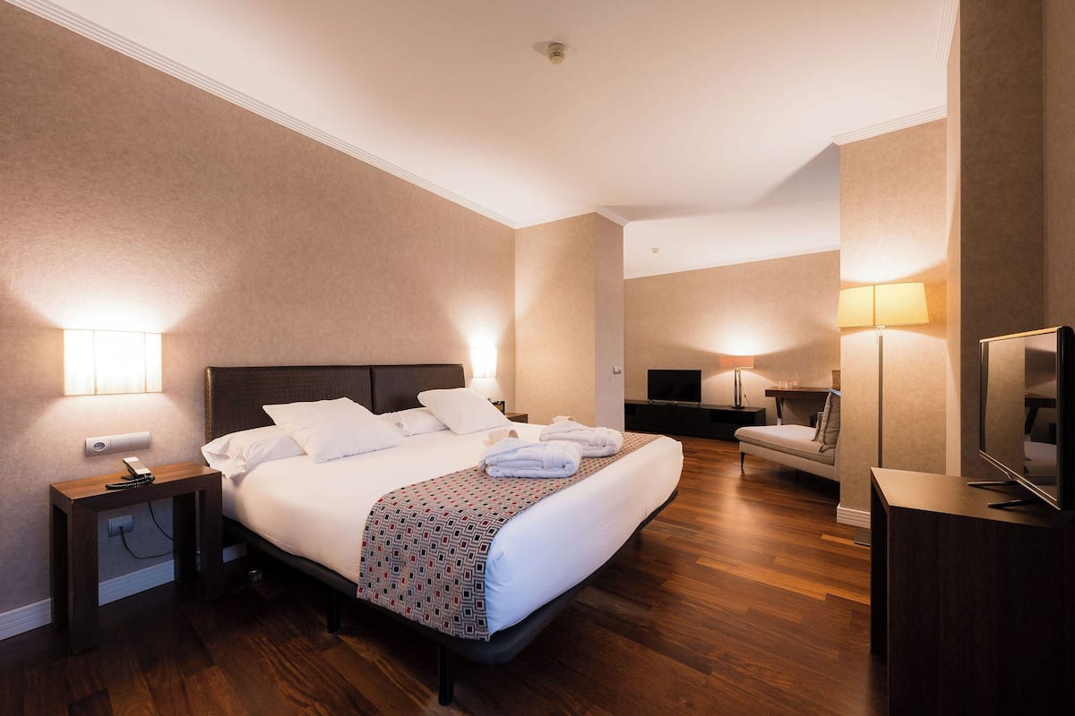 Una habitación de hotel con una cama grande, mesitas de noche, un televisor y un sofá.