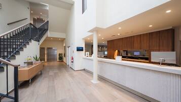 A spacious hotel lobby with a staircase, a reception desk, and a modern kitchen area.