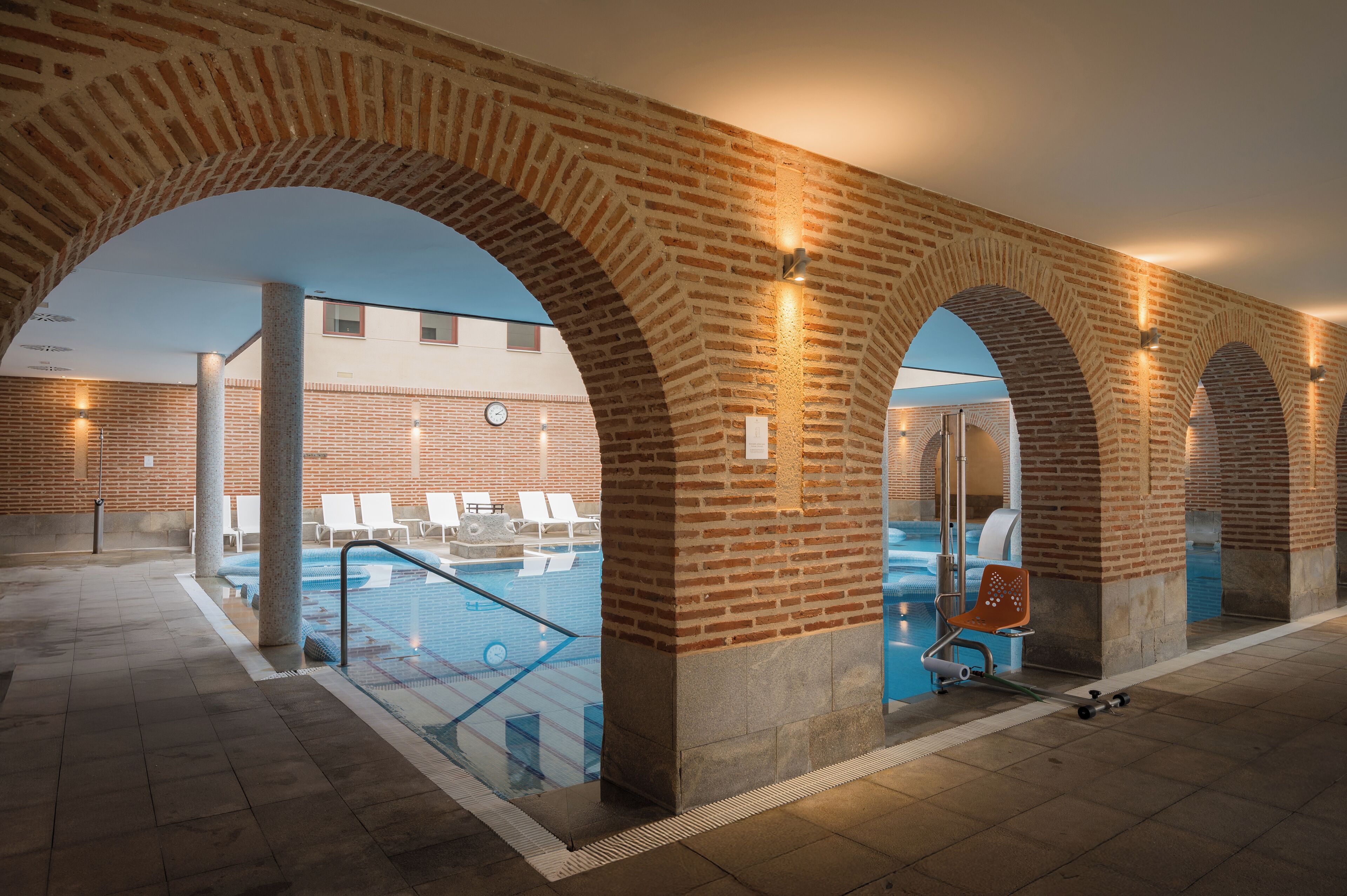 Zona de piscina interior con arcos de ladrillo y sillones de descanso.