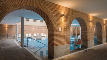 Zona de piscina interior con arcos de ladrillo y sillones de descanso.