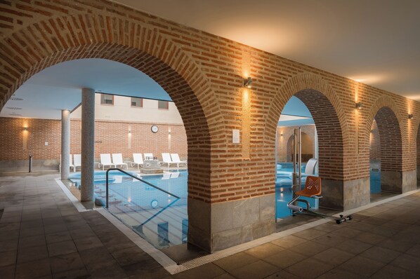 An indoor swimming pool area with brick arches and lounge chairs.