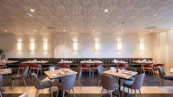 Un restaurante moderno con cabinas y mesas, luces empotradas en el techo y apliques de pared.