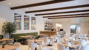 Un restaurant modern amb bigues de fusta, seients amb coixinets verds i una zona de bar.