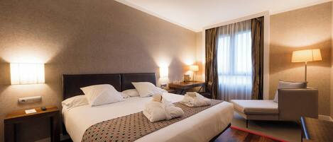 Una habitación de hotel con una cama grande, una mesita de noche, una silla y un escritorio con lámpara.