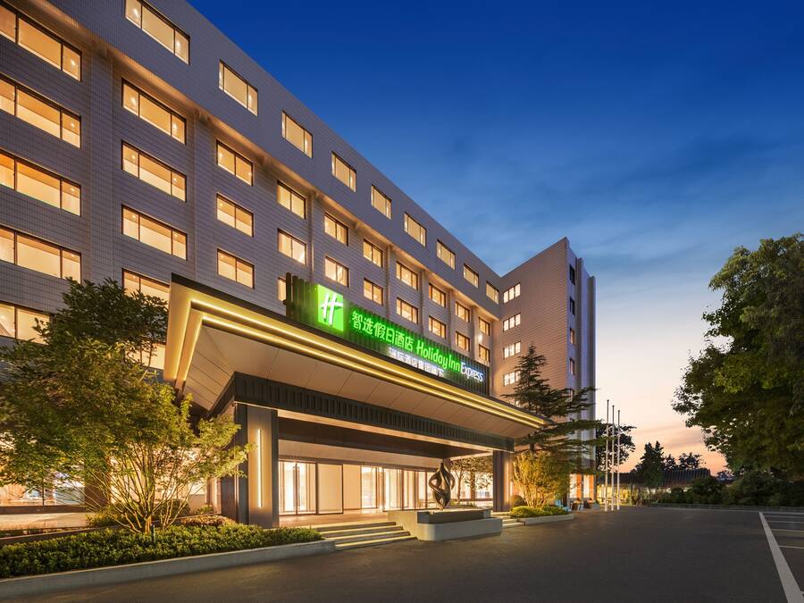 A modern hotel with a prominent green sign, multiple windows, and a well-lit entrance.