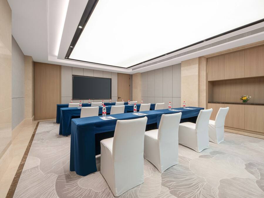 Un salón de conferencias con una larga mesa, sillas blancas y una pantalla grande.