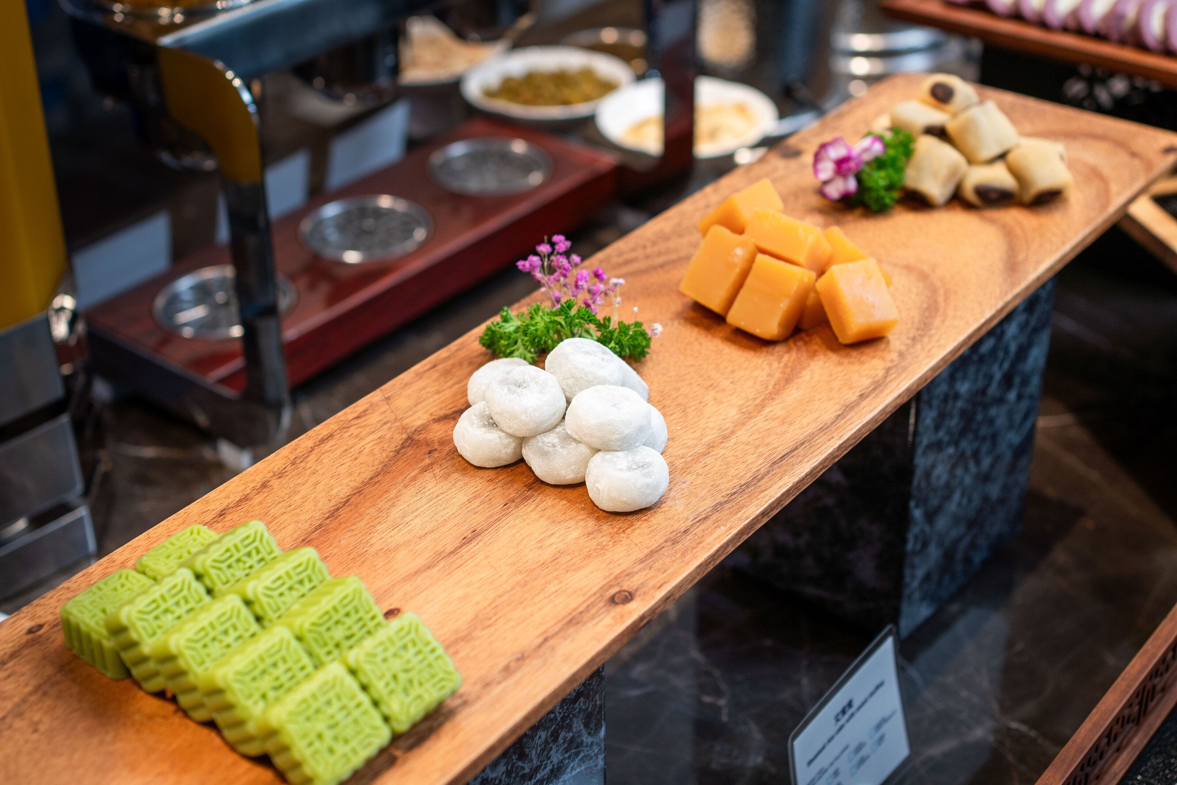 A buffet table with various food items including green and white round pastries, yellow cheese cubes, and other dishes.
