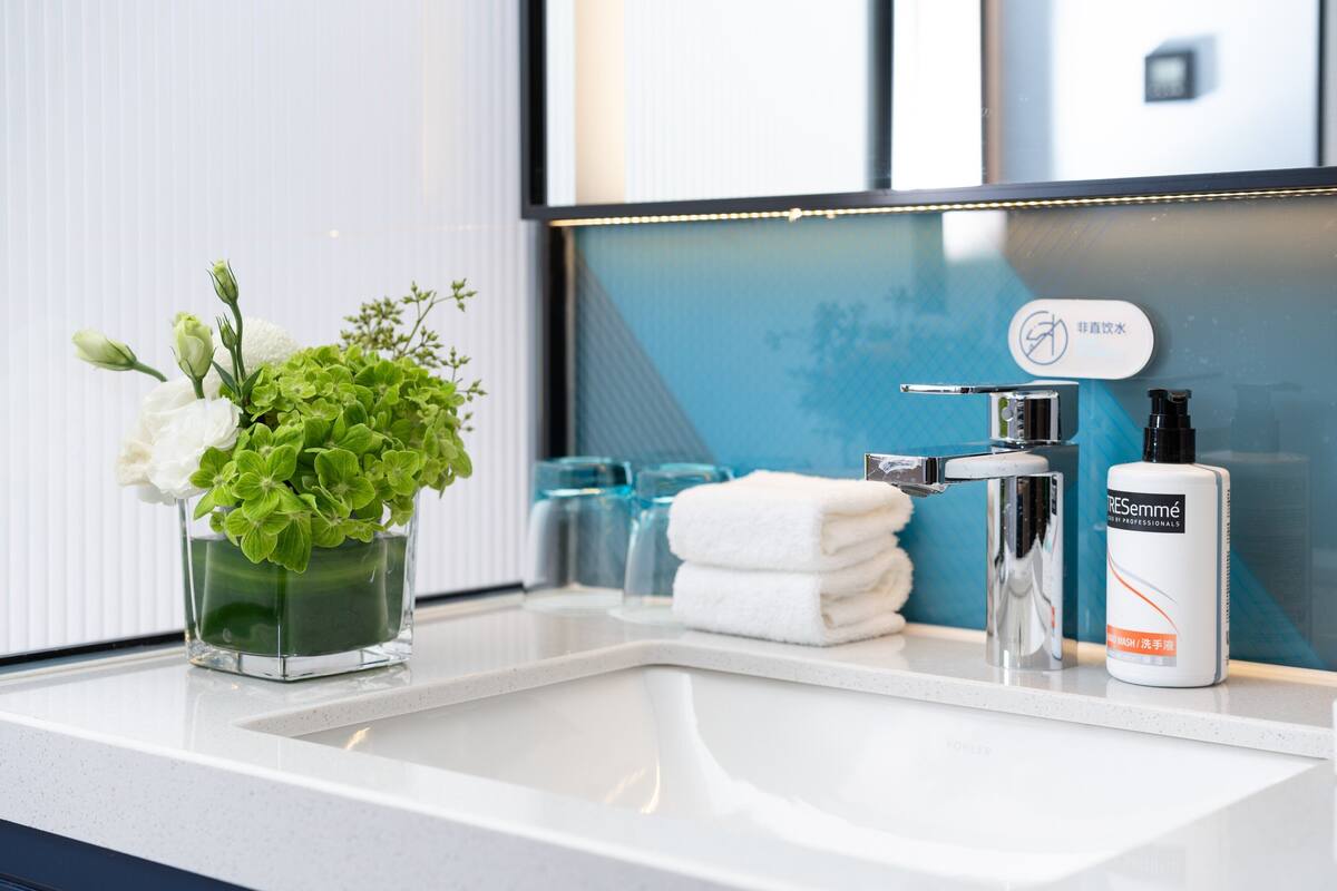 A bathroom sink with a glass vase of flowers, a towel, and a bottle of hand soap.