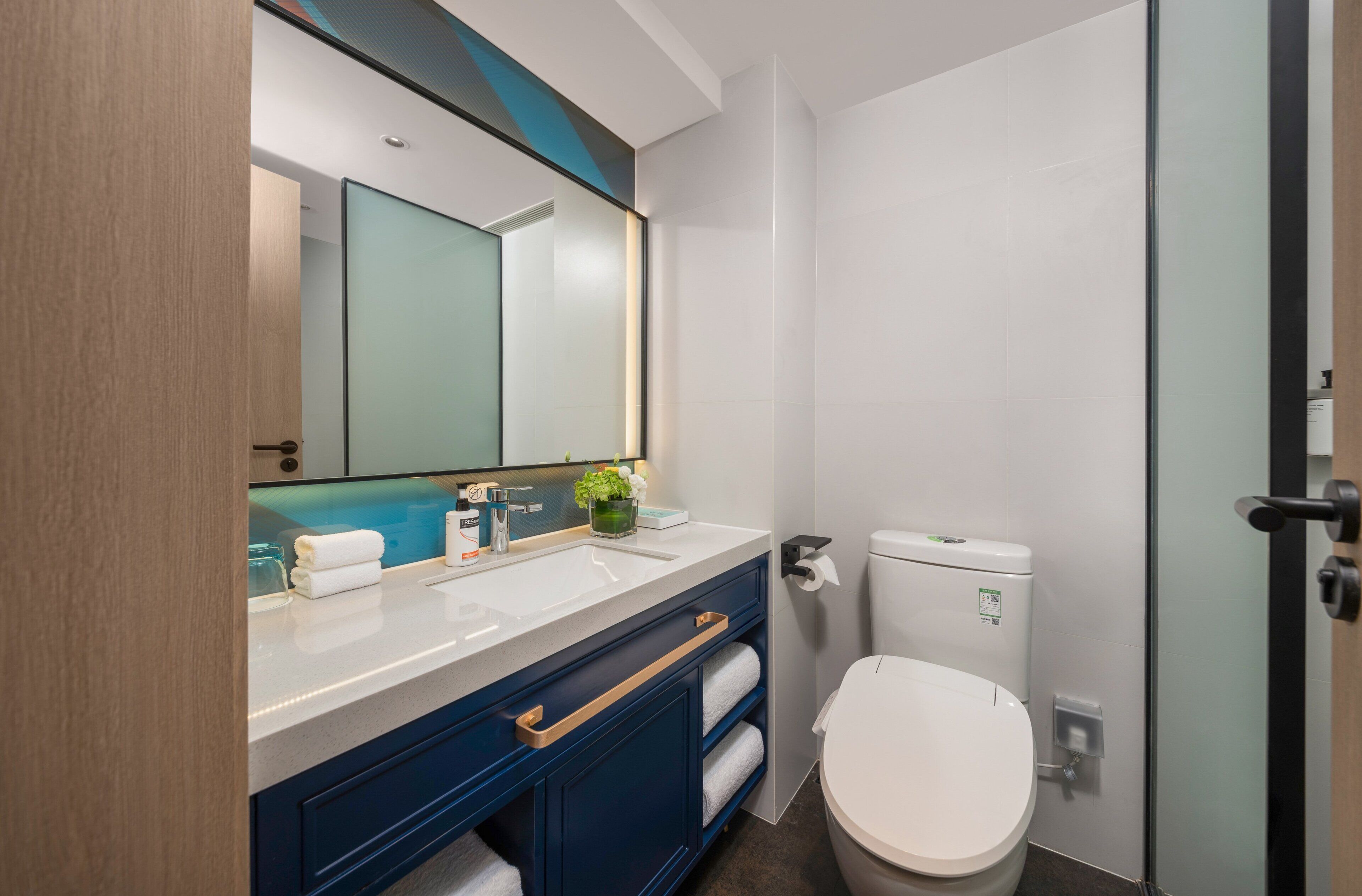 A modern bathroom with a white sink, blue cabinets, a glass shower enclosure, and a white toilet.