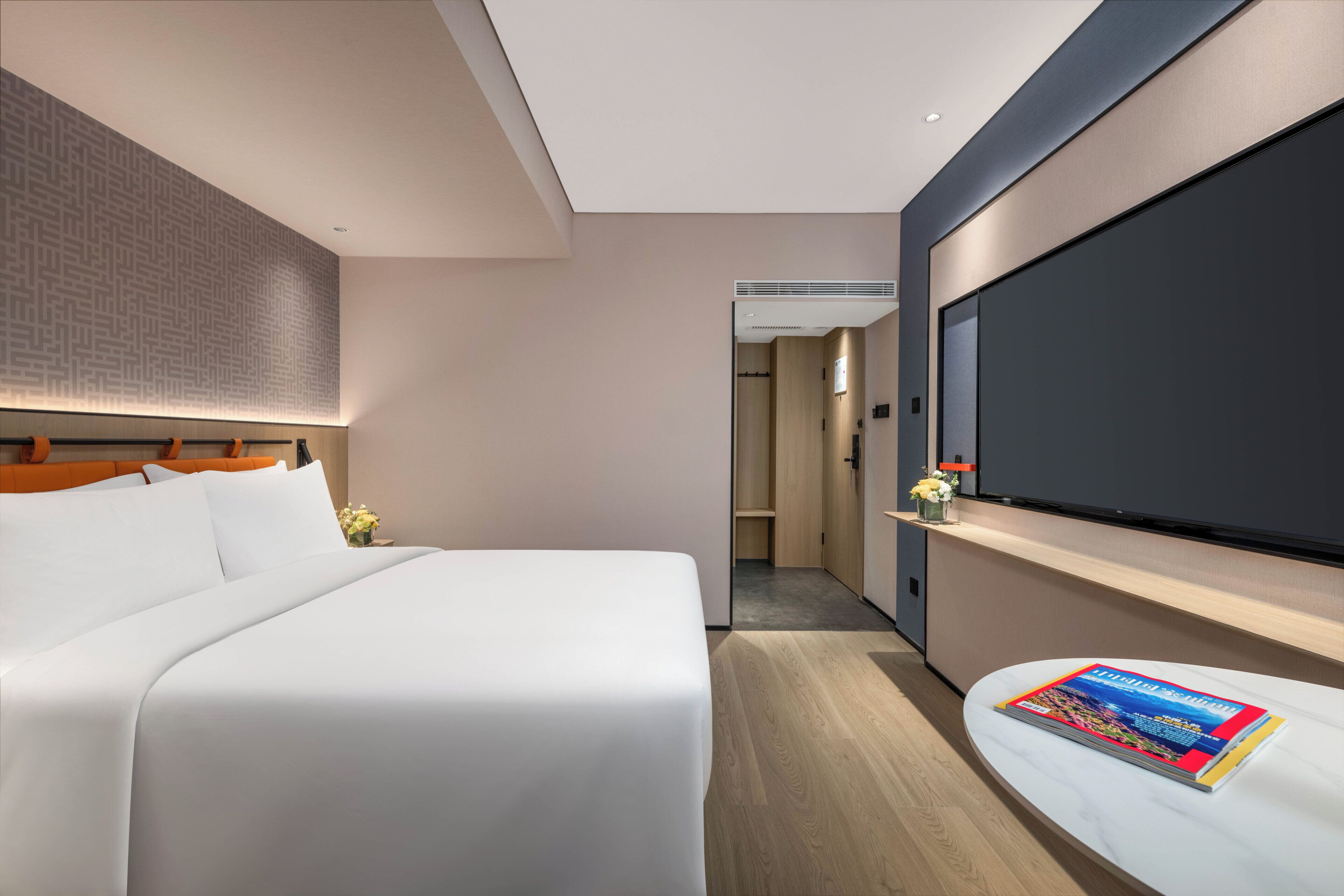 A modern hotel room with a large bed, a flat-screen TV mounted on the wall, and a magazine on the bedside table.