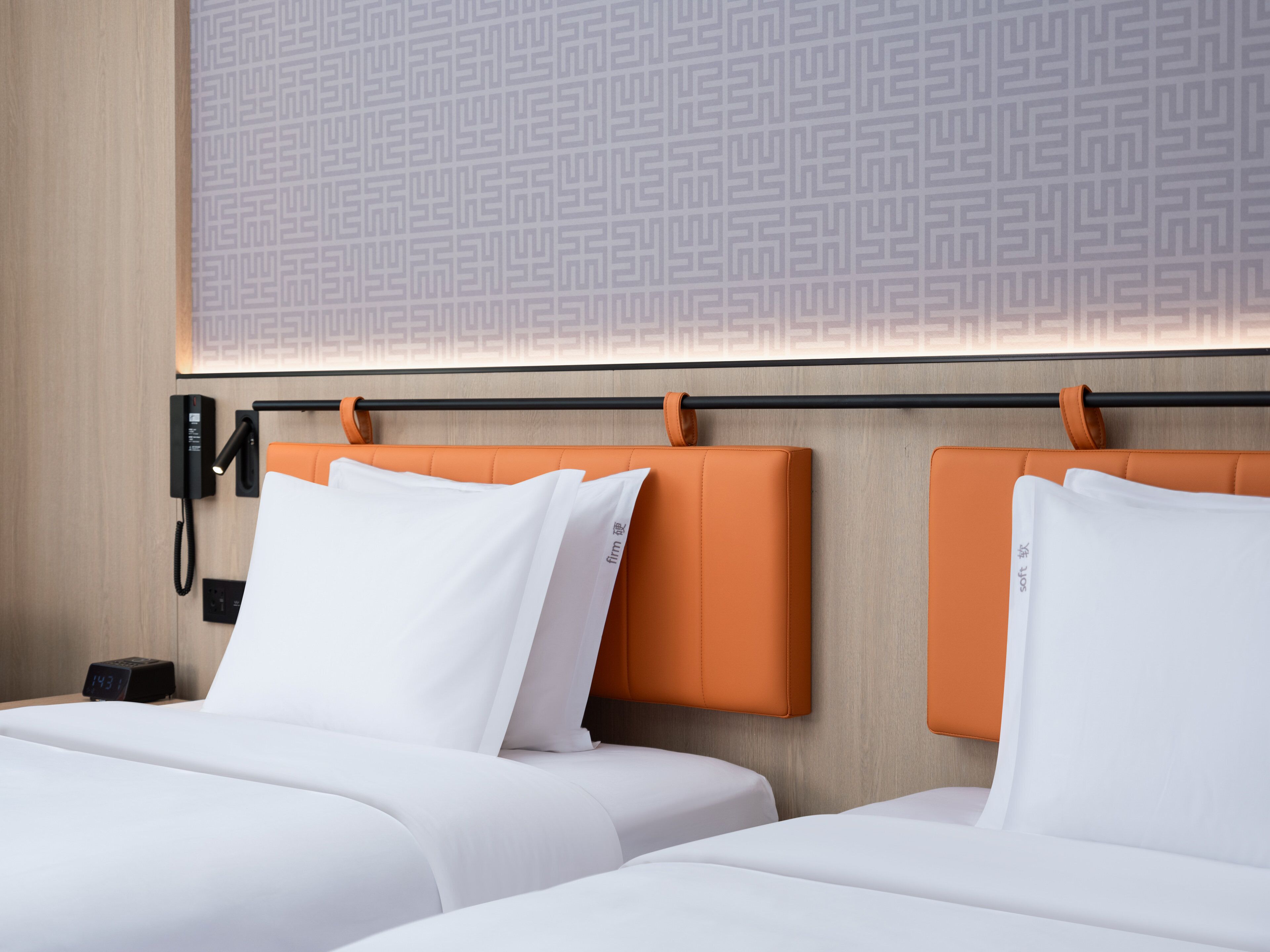 Een hotelkamer met twee bedden, een behang met patroon, een telefoon op het nachtkastje en een klok.