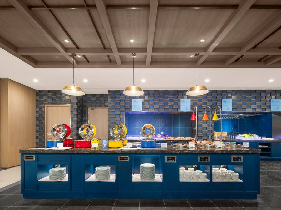 Zona de bufé con mostradores azules, diferentes alimentos e iluminación colgante.