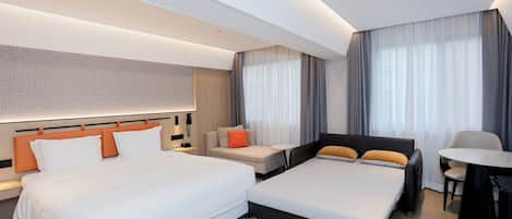 A modern hotel room with two beds, a sofa, a small table, and a desk.