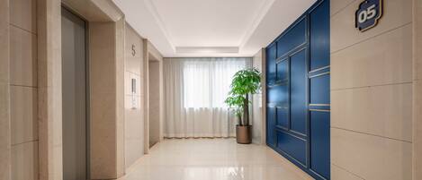 A hallway with a potted plant, a blue door with the number 05, and a white ceiling.