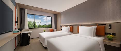 A hotel room with two beds, a desk, a chair, a small table, and a window with a view of buildings.
