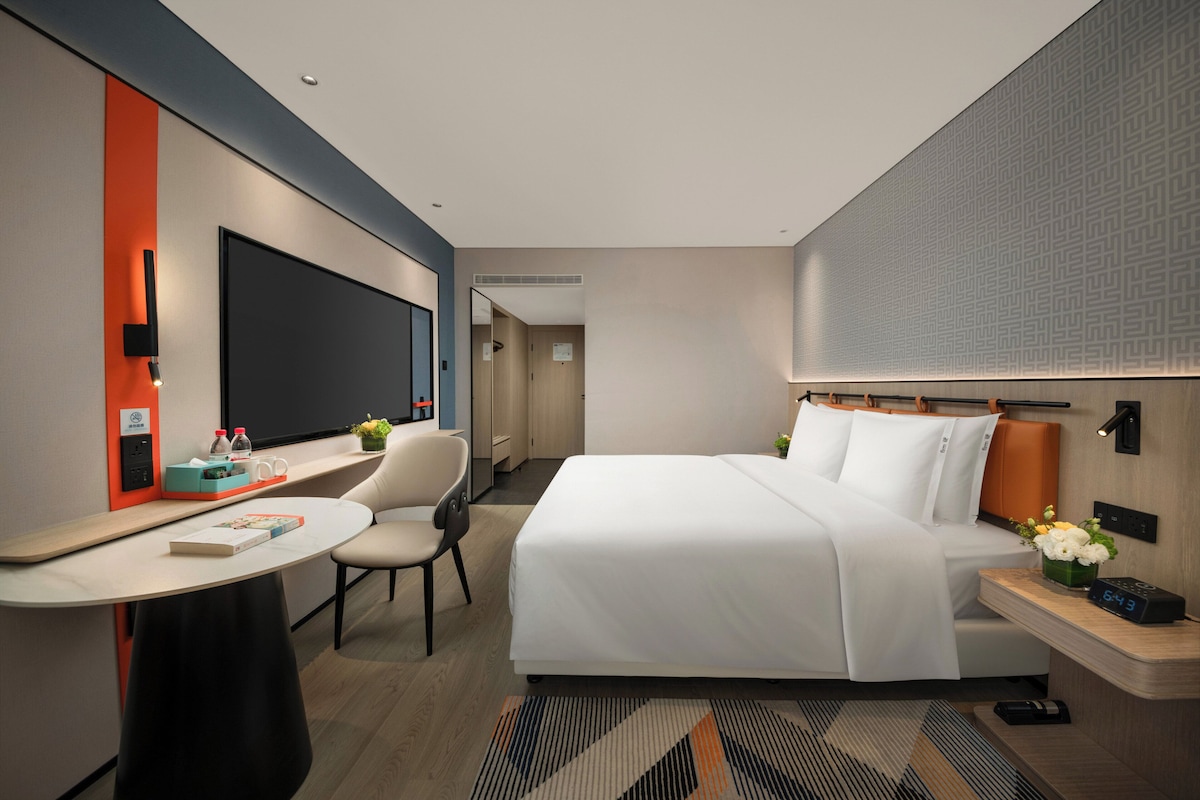A modern hotel room with a bed, desk, chair, and a television.