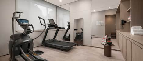 A modern hotel gym with treadmills, a stationary bike, and a small table with water bottles and towels.