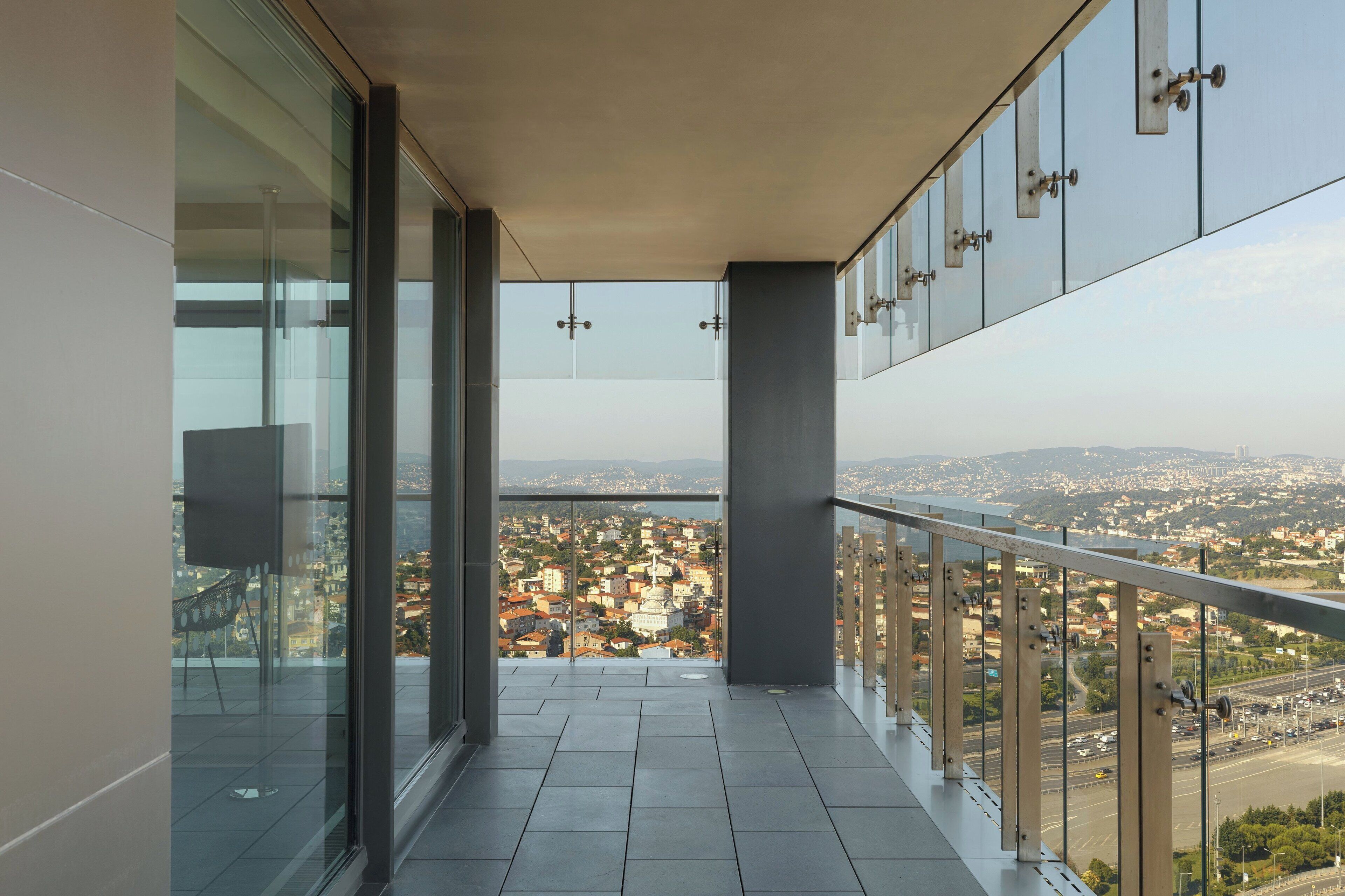 Un balcón con vista a la ciudad, puertas de vidrio y piso de baldosas.