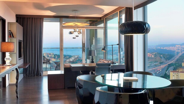 A modern hotel room with a panoramic city view, a glass dining table, and contemporary furniture. - Le Meridien Istanbul Etiler (Istanbul)