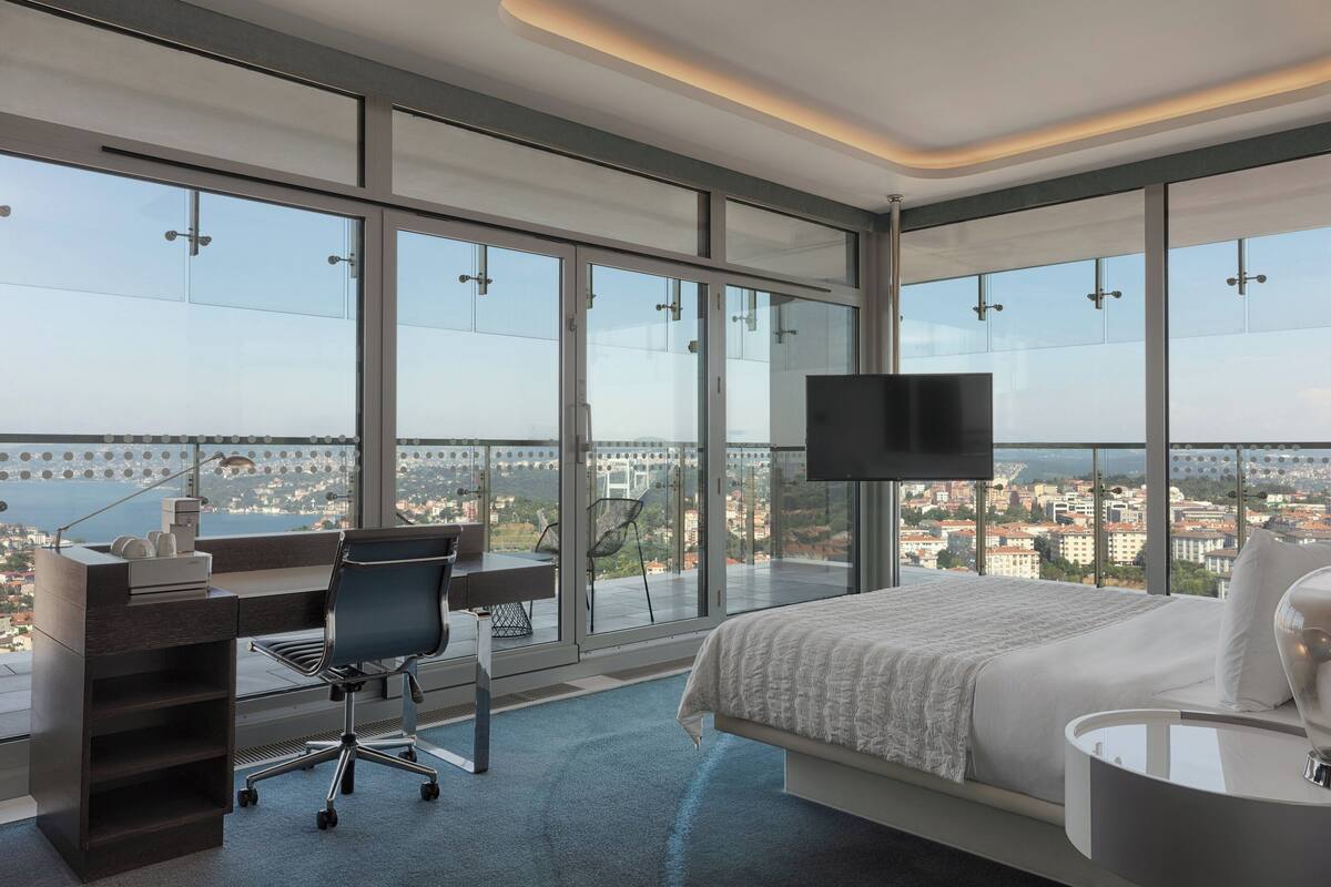 A modern hotel room with a large bed, a desk, and a TV.