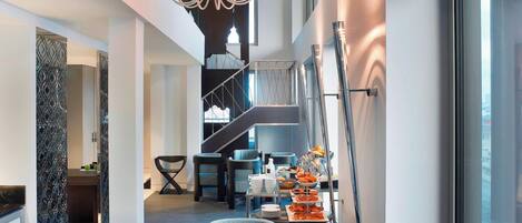 A modern hotel lobby with a staircase, seating area, and a buffet table.