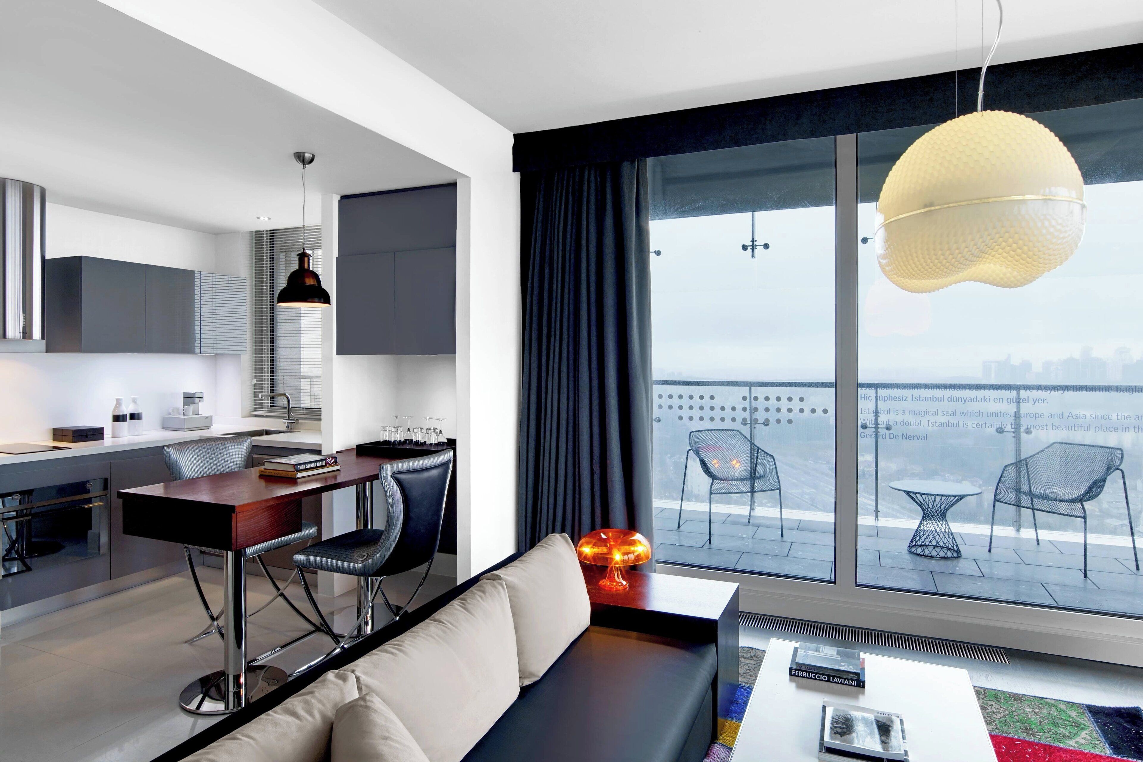 A modern hotel room with a dining area, a sofa, and a large window with a city view.