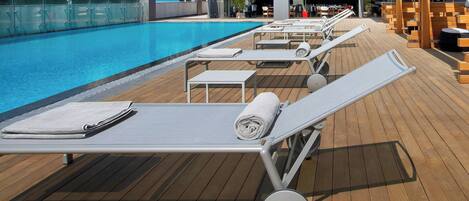 Ein Poolbereich mit Liegestühlen, einer Holzterrasse und einem klaren, blauen Pool.