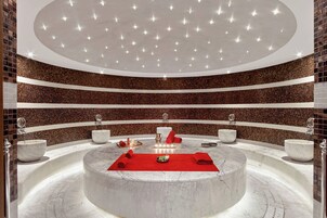 Un'area spa circolare con una vasca idromassaggio centrale, diversi lavabi e un asciugamano rosso sul pavimento.