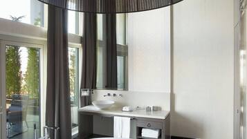 A modern bathroom with a large white bathtub, a round mirror, and a black pendant light.