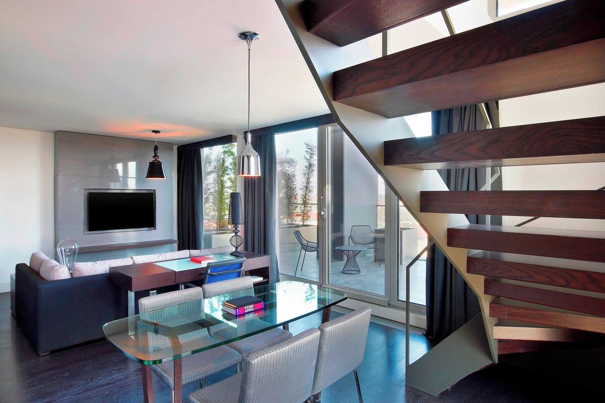 A modern living room with a glass dining table, a sofa, and a TV mounted on the wall.