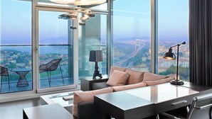 A modern living room with a sofa, a coffee table, and a dining table. There is a large window with a view of a cityscape and a bridge. - Le Meridien Istanbul Etiler (Istanbul)