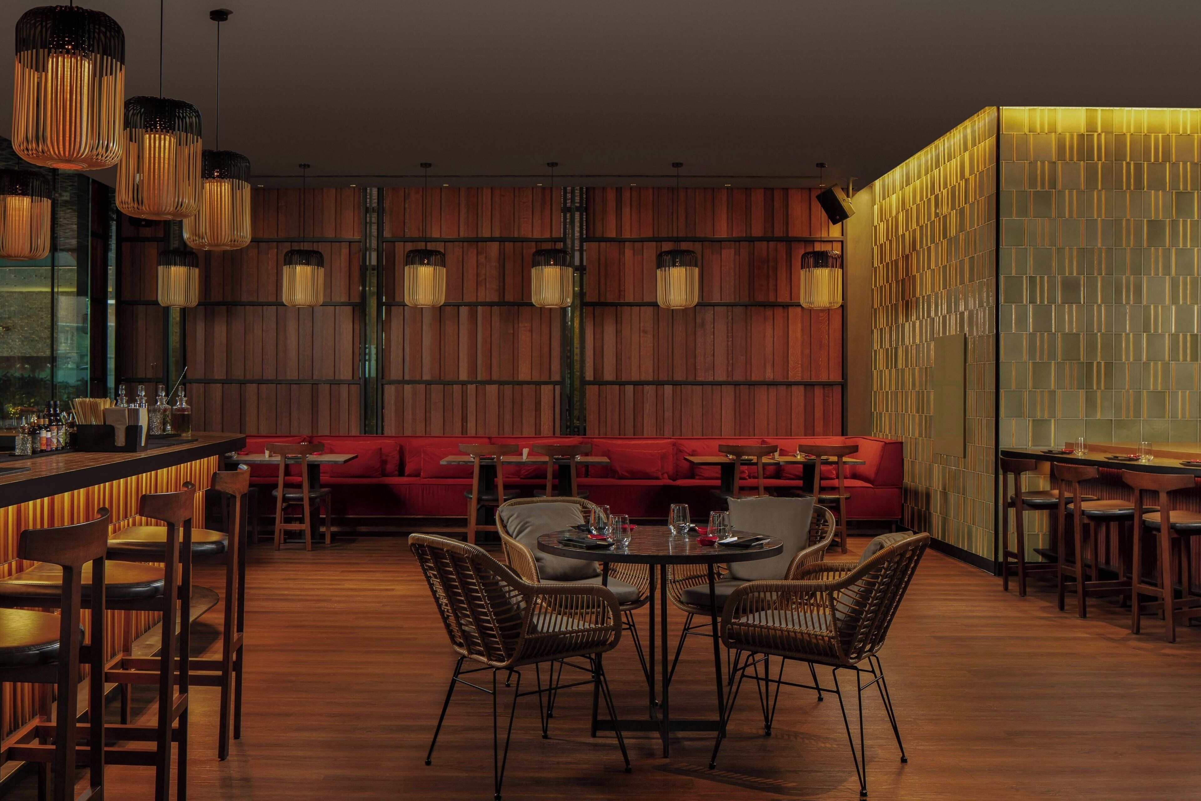 Un restaurante con suelo de madera, mesas redondas, sillas de mimbre y un sofá rojo.