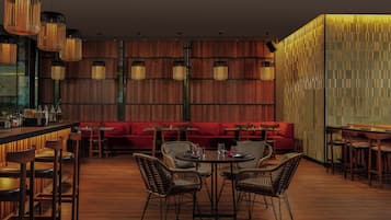 A restaurant with wooden flooring, round tables, wicker chairs, and a red sofa.