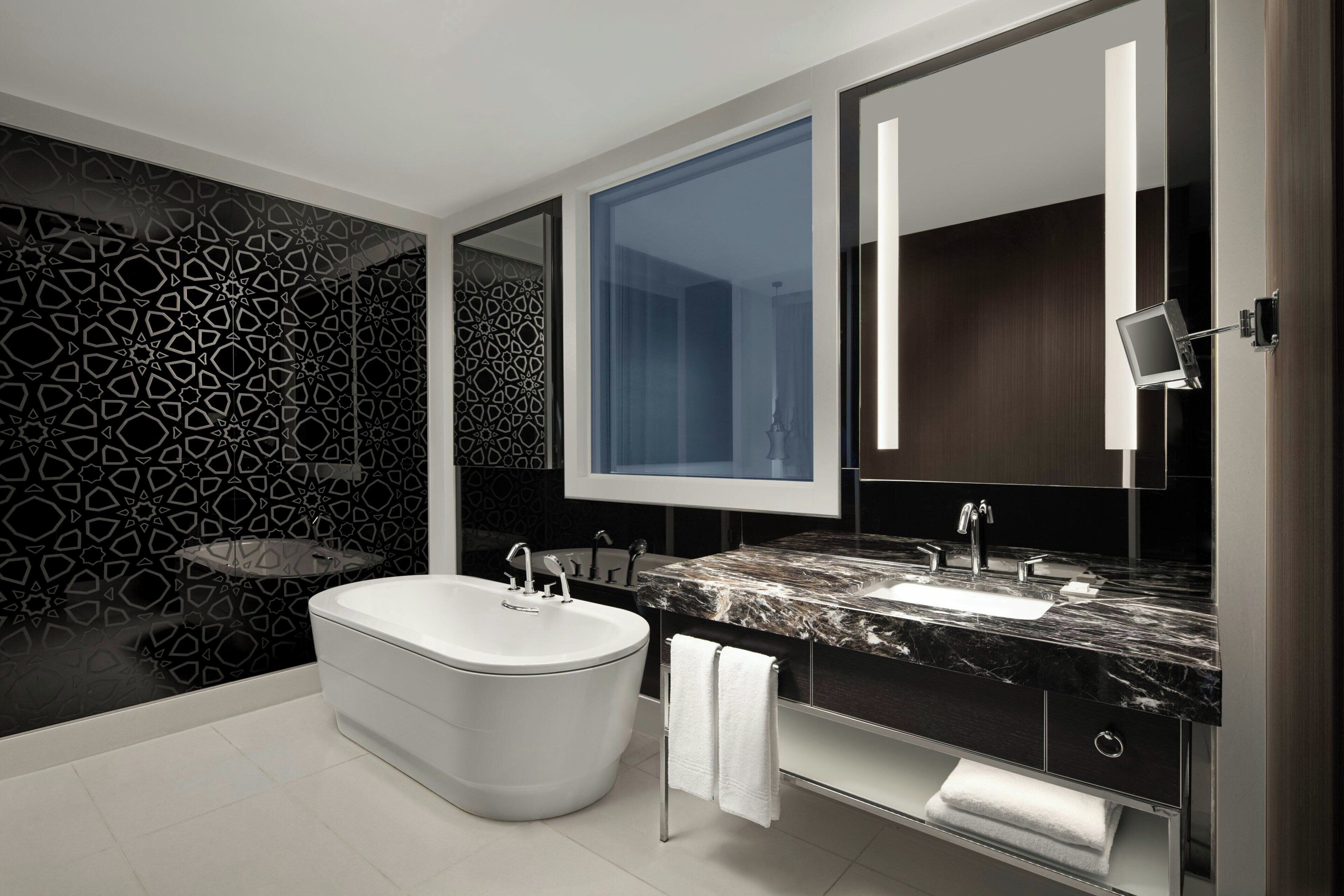 Un baño moderno con una bañera independiente, un espejo grande y una encimera de mármol.
