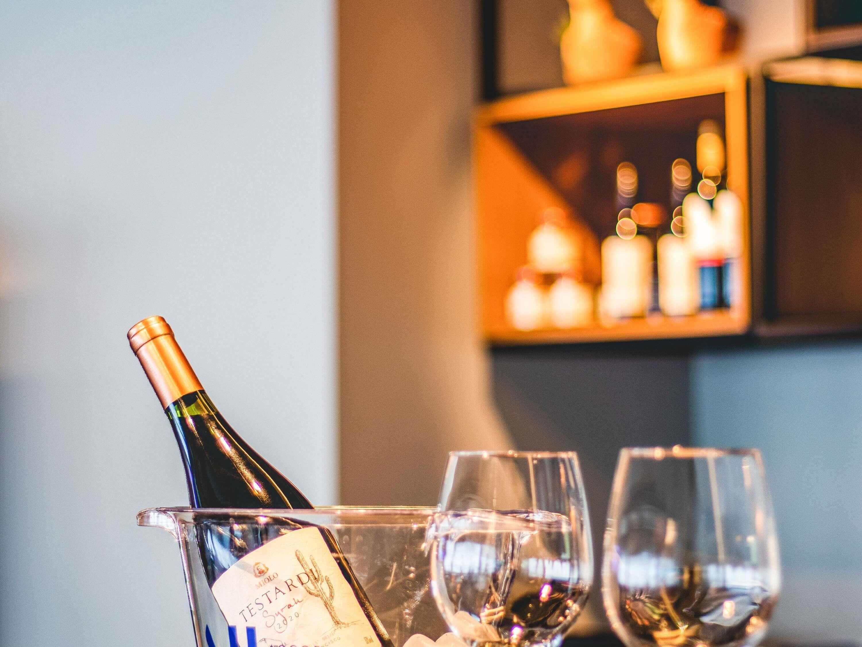 Une bouteille de vin dans un récipient en verre, avec deux verres à vin vides à côté.