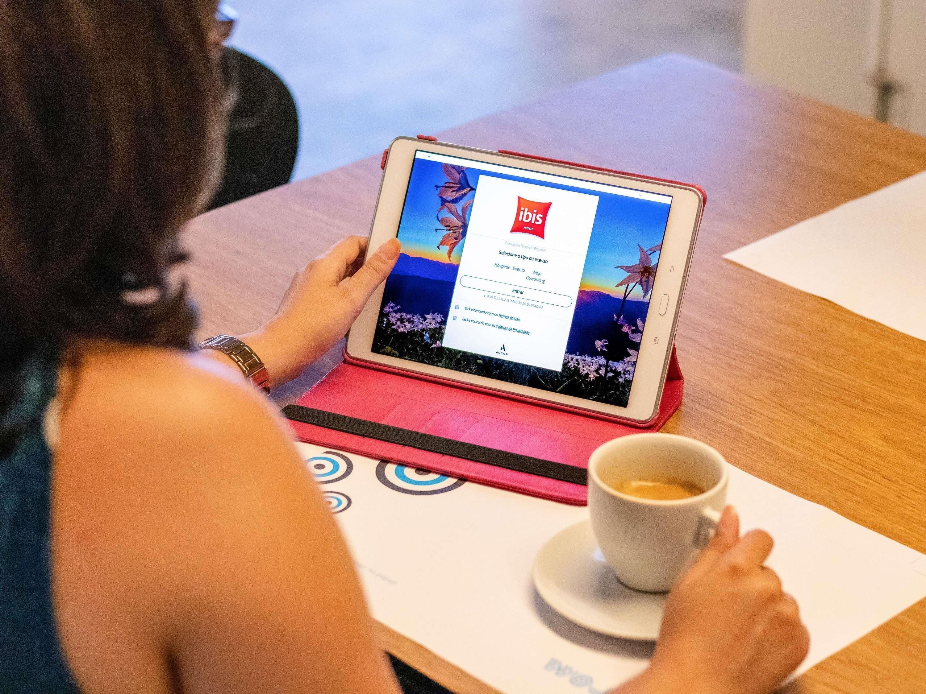 Eine Person benutzt ein Tablet auf einem Holztisch mit einer Kaffeetasse.
