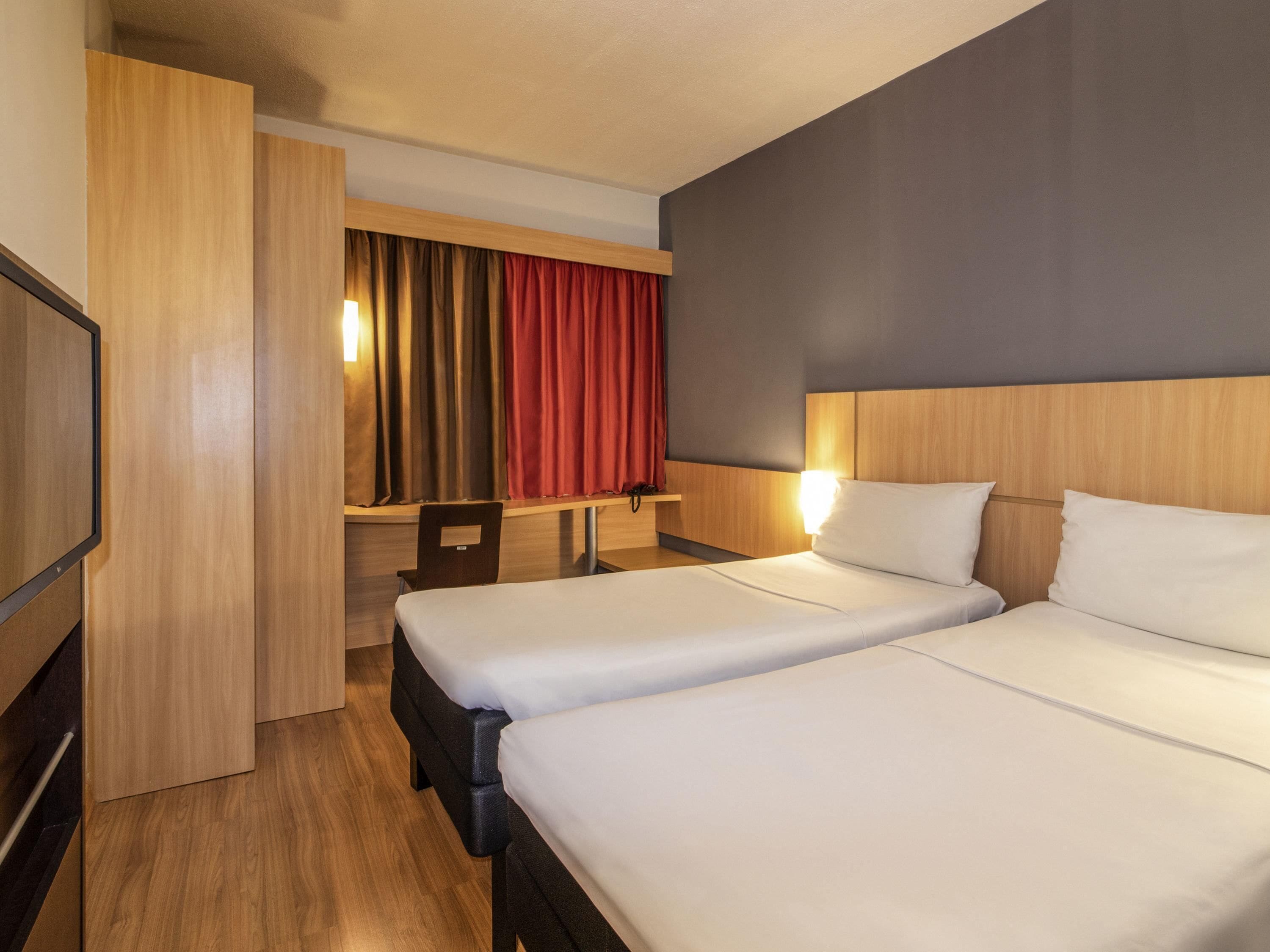 Une chambre d’hôtel avec deux lits, un bureau, une chaise et un téléviseur.