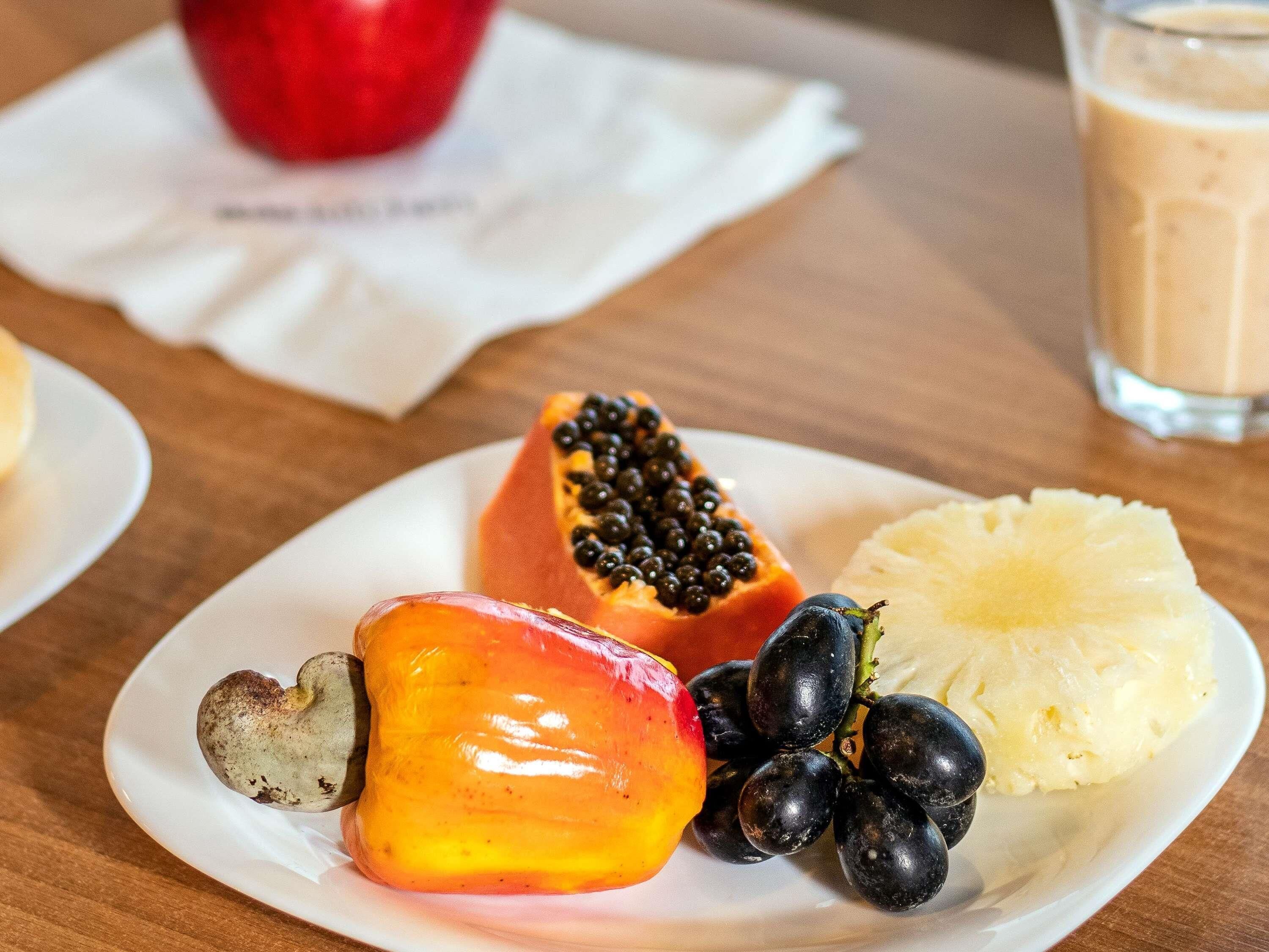 A plate with a halved papaya, a slice of pineapple, and a bunch of black grapes.