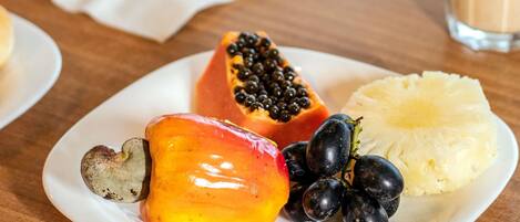 A plate with a halved papaya, a slice of pineapple, and a bunch of black grapes.